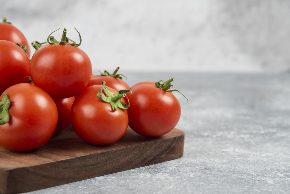 bunch of red fresh tomatoes on wooden cutting board